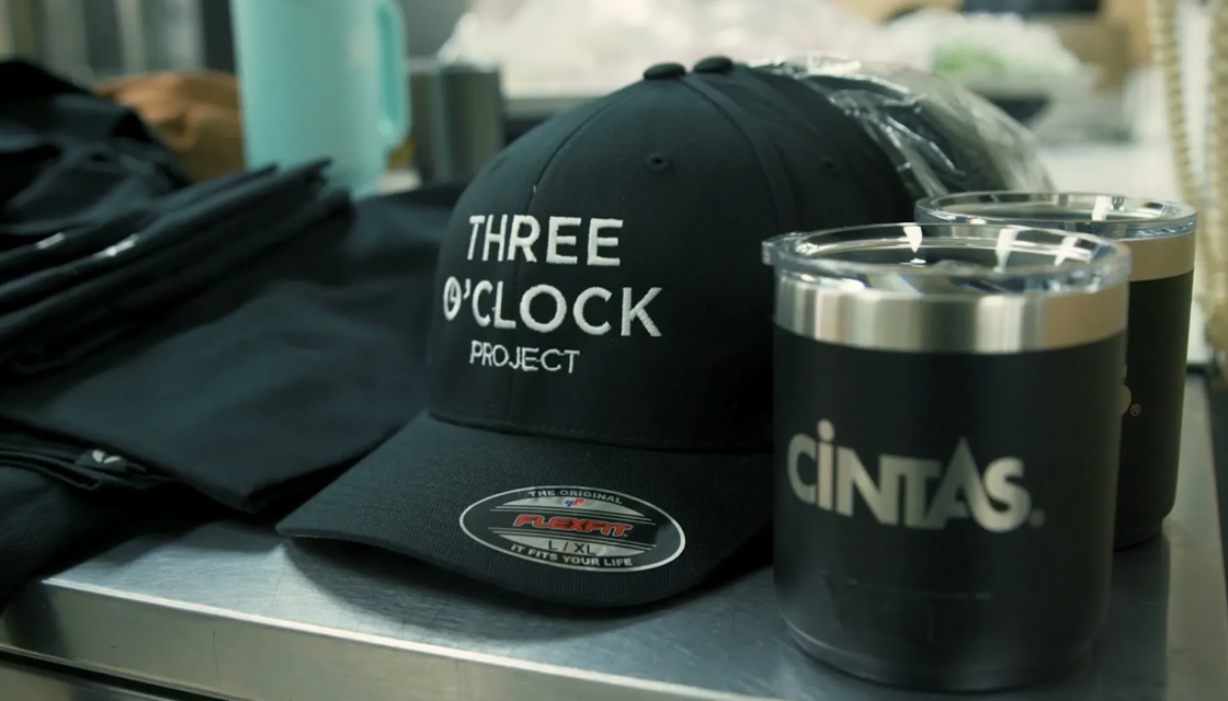 three oclock project hat and cintas mug laying on commerical kitchen service counter