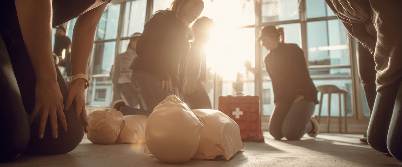 Several people kneel on the floor practicing CPR on training mannequins with a first aid kit in the center | Cintas