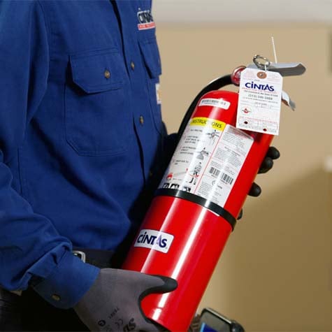 A Cintas technician holding a red fire extinguisher with inspection tags visible.