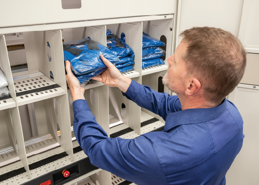 Person retrieves a packaged blue uniform from a self-service dispensing cabinet.