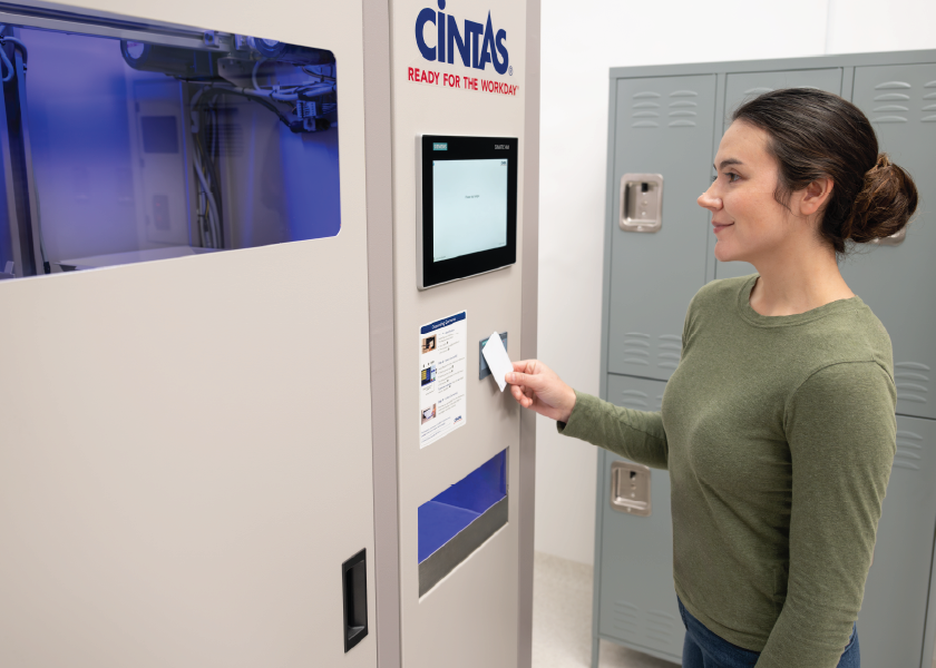 Person scans an access card at a Cintas self-service uniform dispensing machine beside a row of lockers.