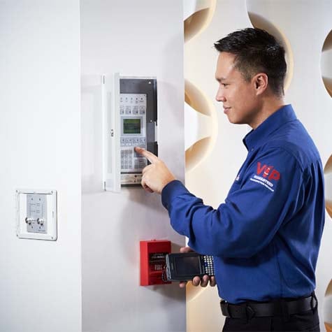 A Cintas Sales Service Representative (SSR) interacting with a wall-mounted fire alarm control panel using a handheld device.