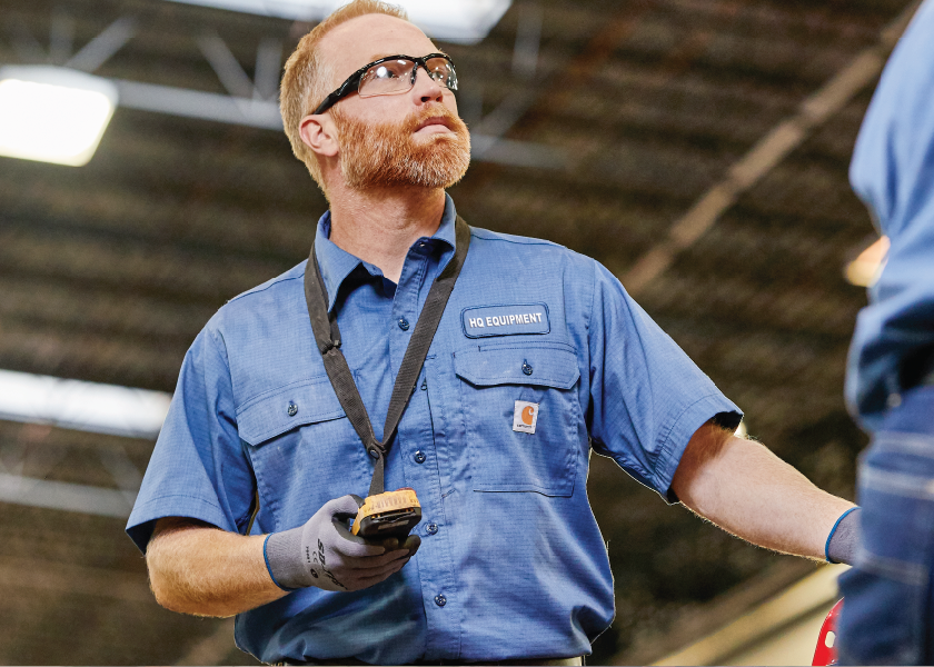 Worker in a blue uniform uses a handheld scanner in an industrial facility.